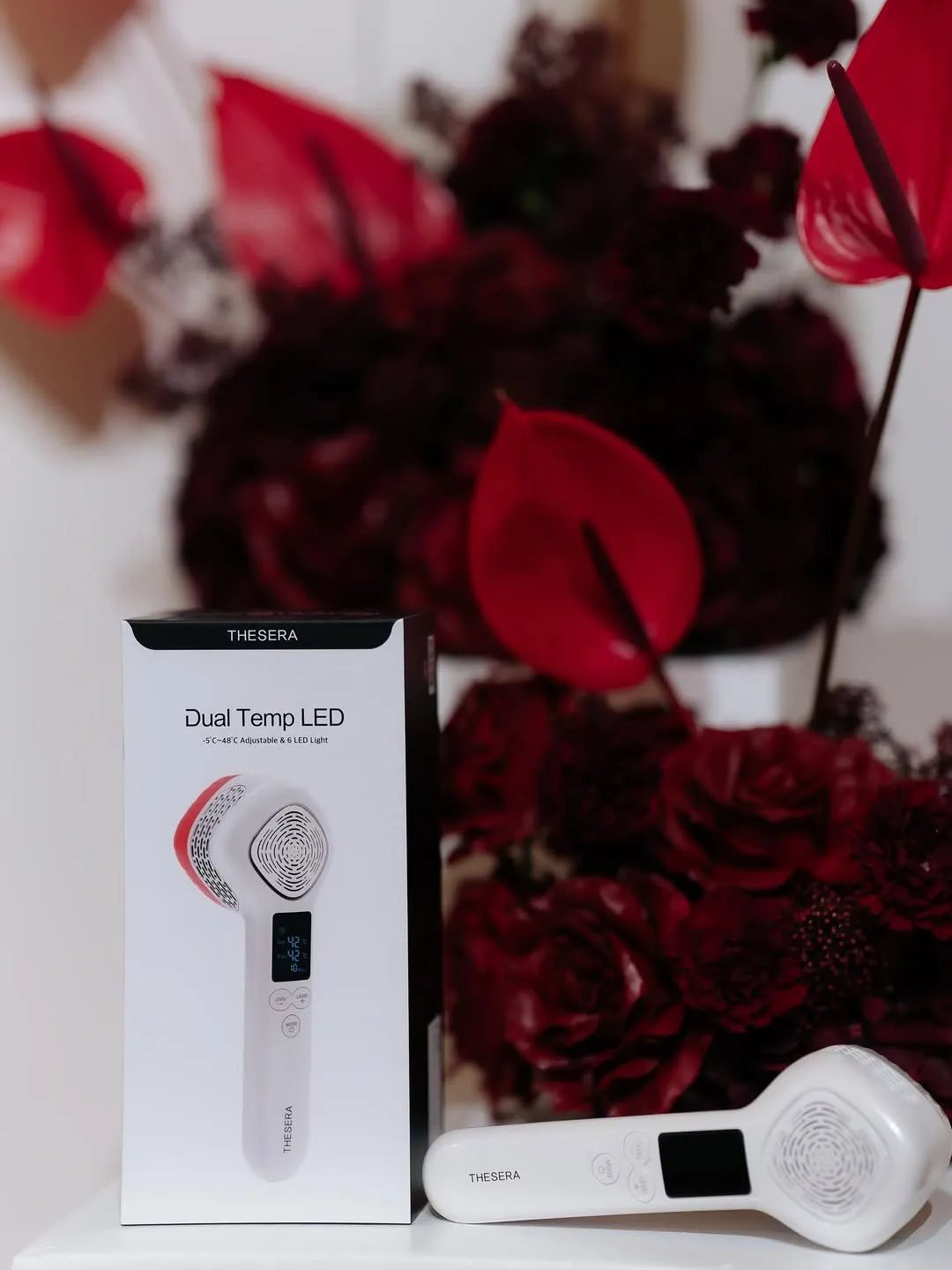 THESERA Dual Temp LED ierīce kabinetā uz tumši sarkanu ziedu fona